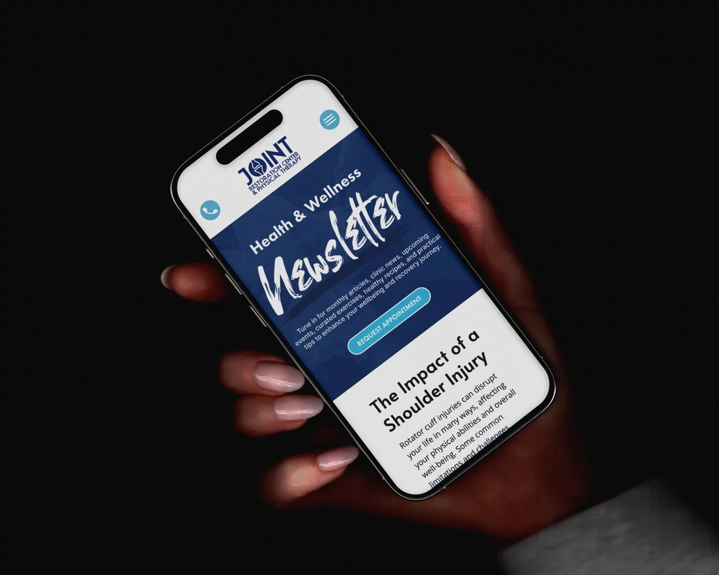 A hand holding a smartphone displaying the Joint Restoration Center & Physical Therapy’s Health & Wellness Newsletter. The screen shows a bold headline, a “Request Appointment” button, and a preview of an article titled “The Impact of a Shoulder Injury.”
