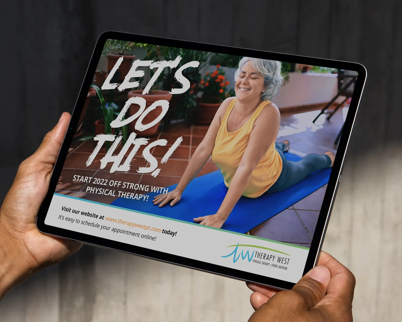 A tablet screen displaying a Therapy West promotional graphic with the bold text “LET’S DO THIS!” and a subheading that reads “Start 2022 off strong with physical therapy.” The image features an older woman in a yellow top and blue leggings smiling while doing a cobra stretch on a yoga mat indoors. Therapy West’s logo and website URL are shown at the bottom.